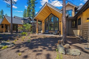 A modern log cabin with a covered patio area, large windows, and a natural surrounding. - NL33B | 56457-2 Elk Run Drive (Sunriver)