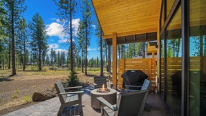 An outdoor patio with a fire pit, seating, and a view of a forest. - NL33A | 56457-1 Elk Run Drive (Sunriver)