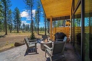 An outdoor patio with a fire pit, seating, and a view of a forest. - NL33A | 56457-1 Elk Run Drive (Sunriver)