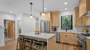 A modern kitchen with wooden cabinets, a stainless steel refrigerator, a built-in oven, and a large window offering a view of trees. - NL33A | 56457-1 Elk Run Drive (Sunriver)