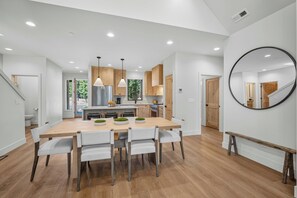 A modern kitchen with wooden cabinets, a stainless steel refrigerator, pendant lights, and a dining area with a wooden table and chairs. - NL33A | 56457-1 Elk Run Drive (Sunriver)