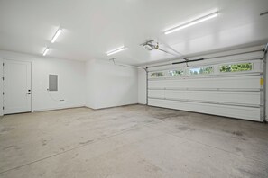 A clean, empty garage with a white door, fluorescent lighting, and a large garage door. - NL33A | 56457-1 Elk Run Drive (Sunriver)