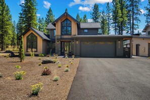 A two-story house with a garage, surrounded by a landscaped garden with various plants and a driveway. - NL33A | 56457-1 Elk Run Drive (Sunriver)