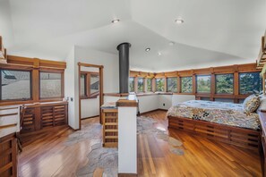 Ein Schlafzimmer mit einem großen Bett, Holzmöbeln, Steinfußboden und mehreren Fenstern.
