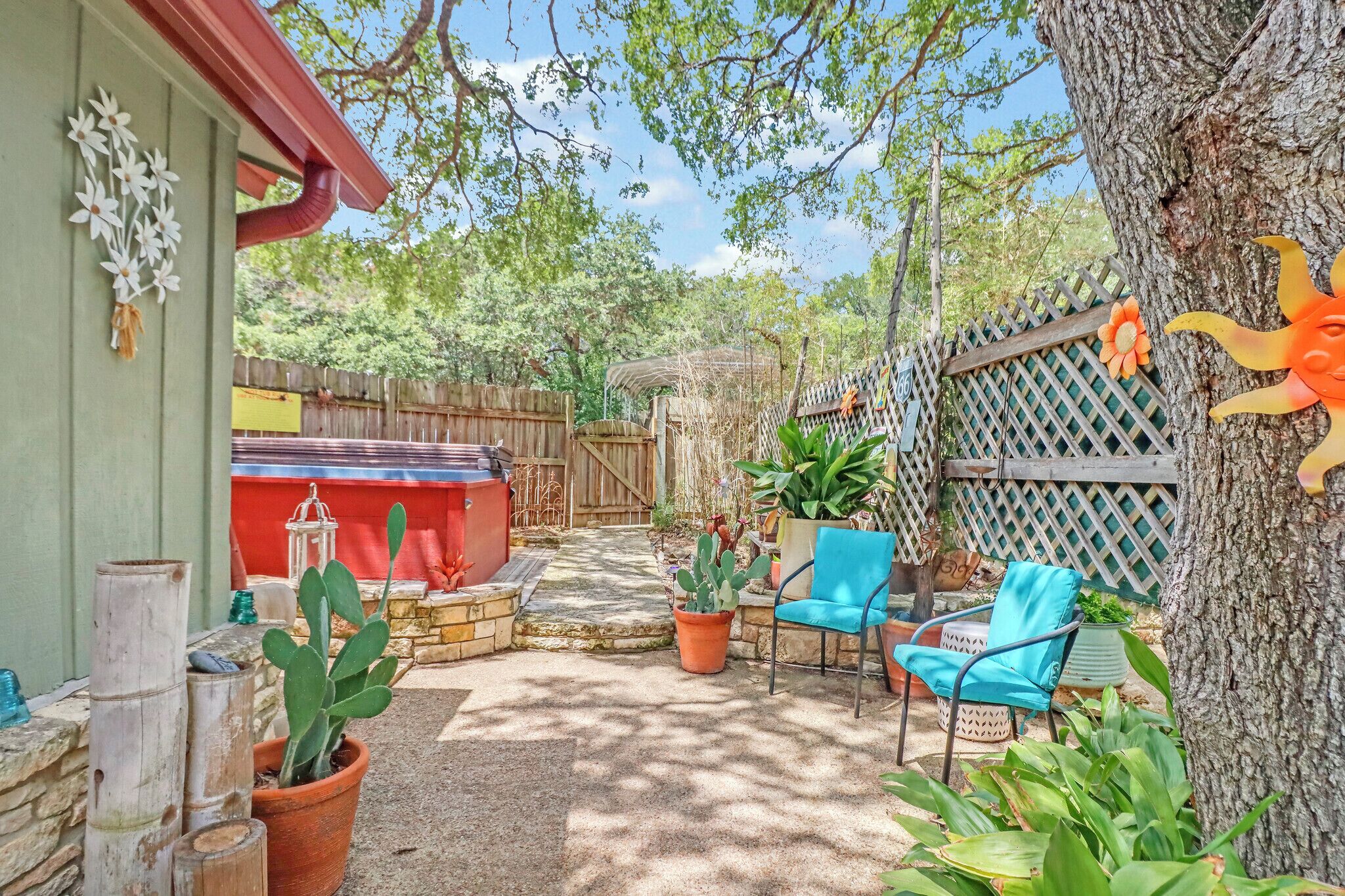 A patio area with a wooden fence, a cactus plant, a blue chair, and a tree.