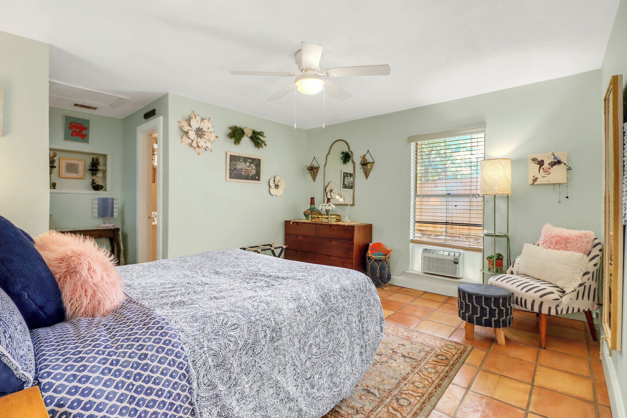 A bedroom with a bed, a dresser, a chair, a window with blinds, and a ceiling fan.