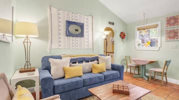Una sala de estar con un sofá azul, una mesa de centro de madera y un comedor con una mesa pequeña y sillas.