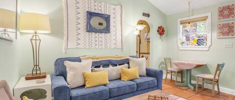 A living room with a blue sofa, a wooden coffee table, and a dining area with a small table and chairs.