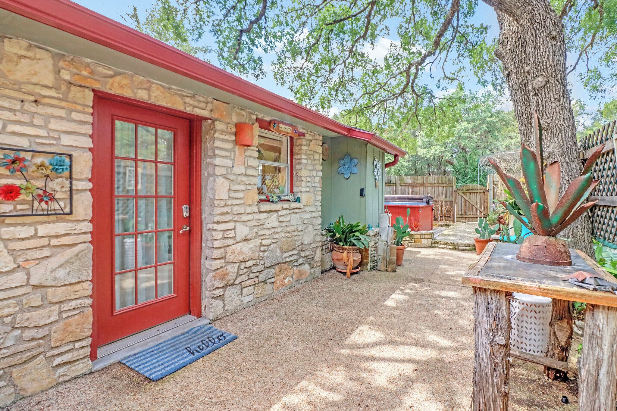A stone house with a red door, a blue mat with 'hello' on it, and potted plants.