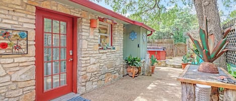 A stone house with a red door, a blue mat with 'hello' on it, and potted plants.