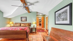 Ein Schlafzimmer mit einem Bett, Nachttischlampen, einem Deckenventilator, einem gerahmten Bild und einer hölzernen Bank.