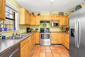 A kitchen with wooden cabinets, a stainless steel refrigerator, a microwave, and a stove. - Hillsedge Haciendas | Multi unit Hill Country Retreat with Hot Tubs (Wimberley)
