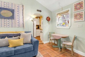 A living room with a blue sofa, a dining table with chairs, a kitchen in the background, and a wall with a decorative mirror and artwork. - Hillsedge Haciendas | Multi unit Hill Country Retreat with Hot Tubs (Wimberley)