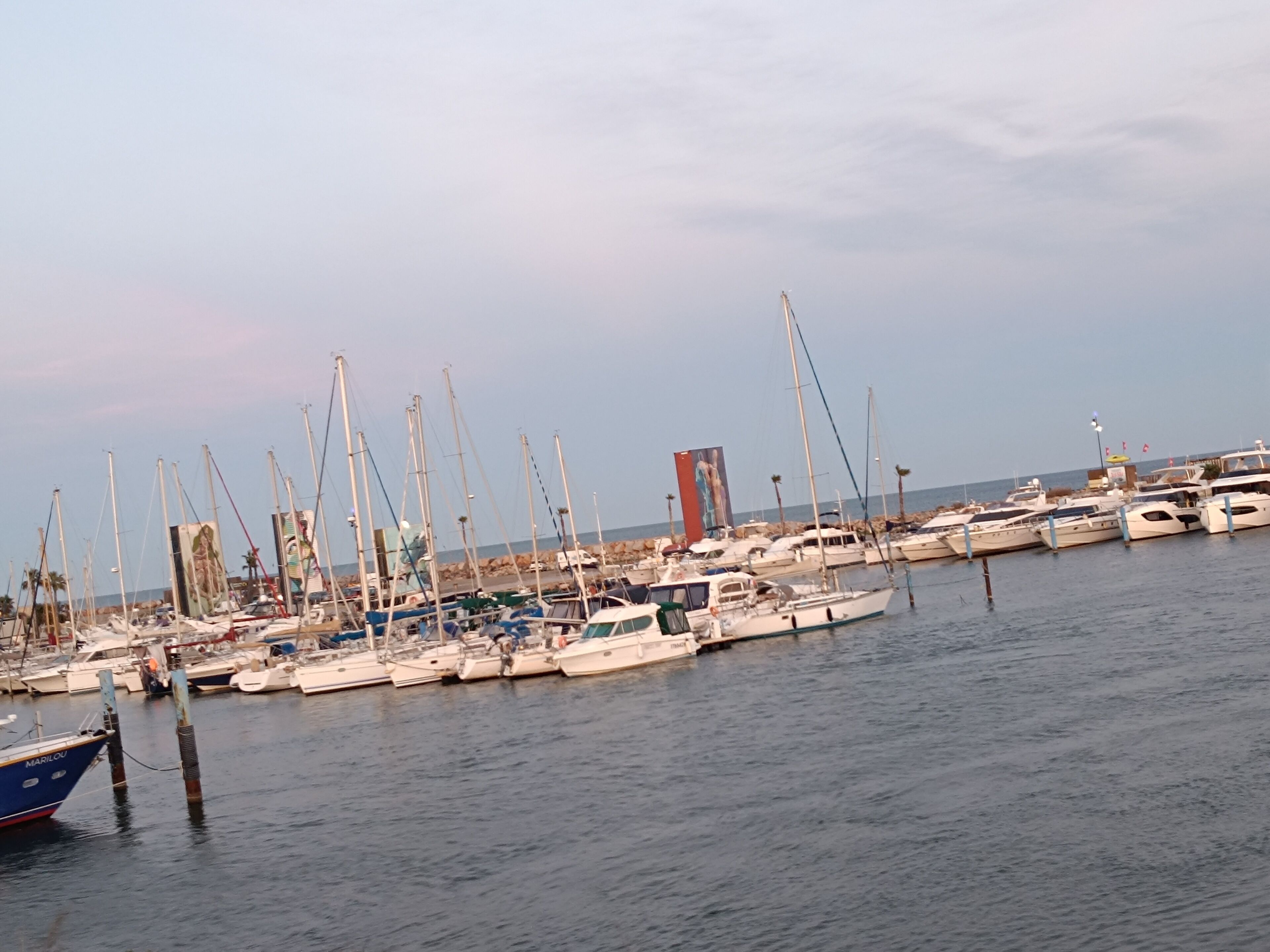 A marina with multiple boats docked, a clear sky, and calm water.