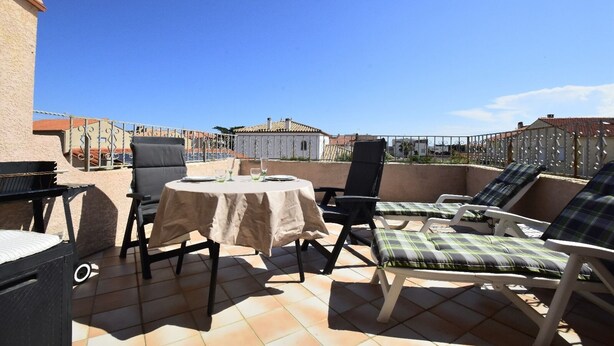 A rooftop terrace with a round table, chairs, and lounge seating. - Air-conditioned apartment with a pool and a large terrace on the waterfront (Le Barcarès)