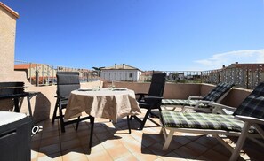 A rooftop terrace with a round table, chairs, and lounge seating. - Air-conditioned apartment with a pool and a large terrace on the waterfront (Le Barcarès)