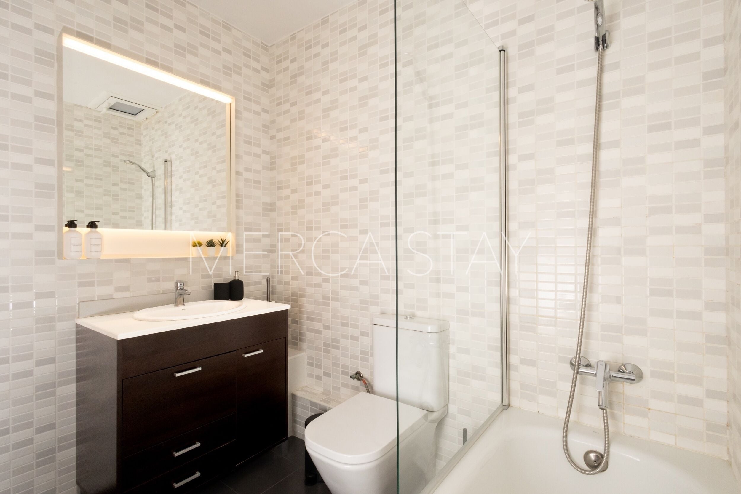 Un bagno moderno con cabina doccia in vetro, un WC bianco e un mobile lavabo scuro con specchio.