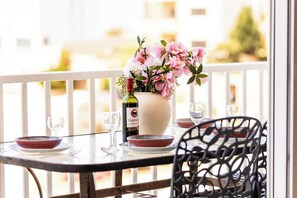 Ein Tisch mit einer Blumenvase, einer Weinflasche und zwei Gläsern auf einem Balkon mit Geländer.