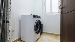 Una lavanderia piccola e compatta, con lavatrice, un cestino e una porta che dà su un'altra stanza.