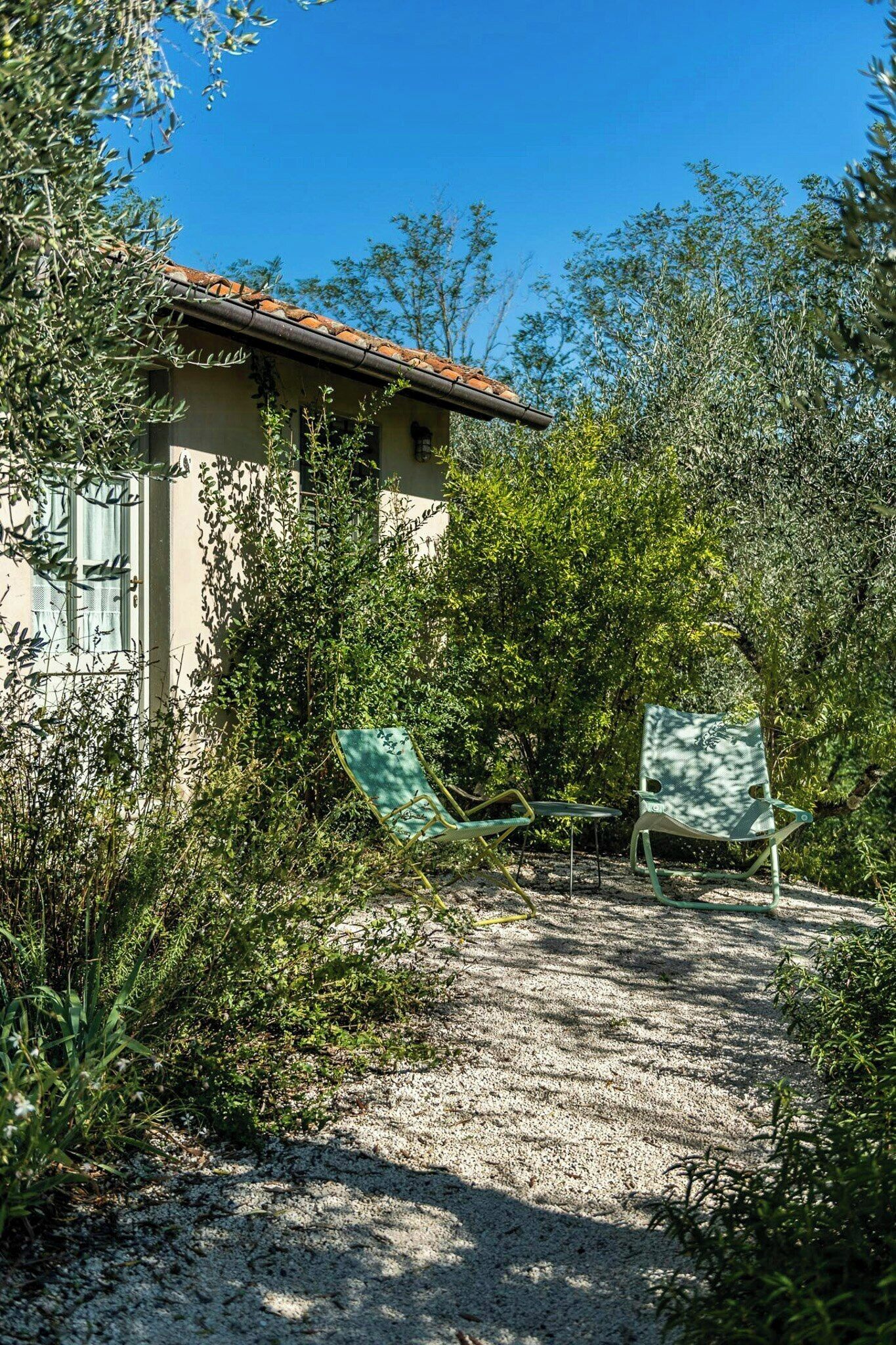 Un bâtiment doté d’un toit en tuiles, entouré d’une végétation luxuriante, avec deux chaises pliantes vertes à proximité.