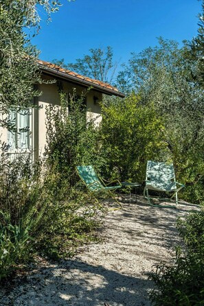 A building with a tiled roof, surrounded by dense vegetation and two green folding chairs. - Apartment in farmstead with olive groves and pool (Buggiano)