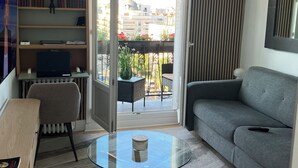 Een moderne woonkamer met een bank, een glazen salontafel, een boekenkast en uitzicht op de stad door een groot raam.
