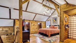 Ein gemütliches Schlafzimmer im Dachgeschoss mit Holzbalkendecke, einem Bett, einem Schreibtisch und einem Fenster.