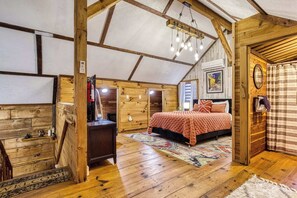 Ein gemütliches Schlafzimmer im Dachgeschoss mit Holzbalkendecke, einem Bett, einem Schreibtisch und einem Fenster.