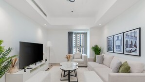 Ein modernes Wohnzimmer mit Flachbildfernseher, einem weißen Sofa, einem Couchtisch und einem großen Fenster mit Vorhängen.