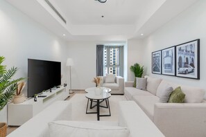 Ein modernes Wohnzimmer mit Flachbildfernseher, einem weißen Sofa, einem Couchtisch und einem großen Fenster mit Vorhängen.