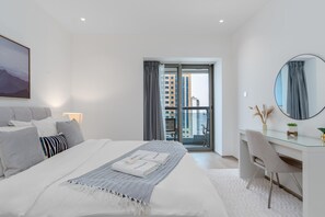 Ein modernes Hotelzimmer mit einem großen Bett, einem Schreibtisch, einem Sessel, einem runden Spiegel und Blick auf die Stadt durch das Fenster.