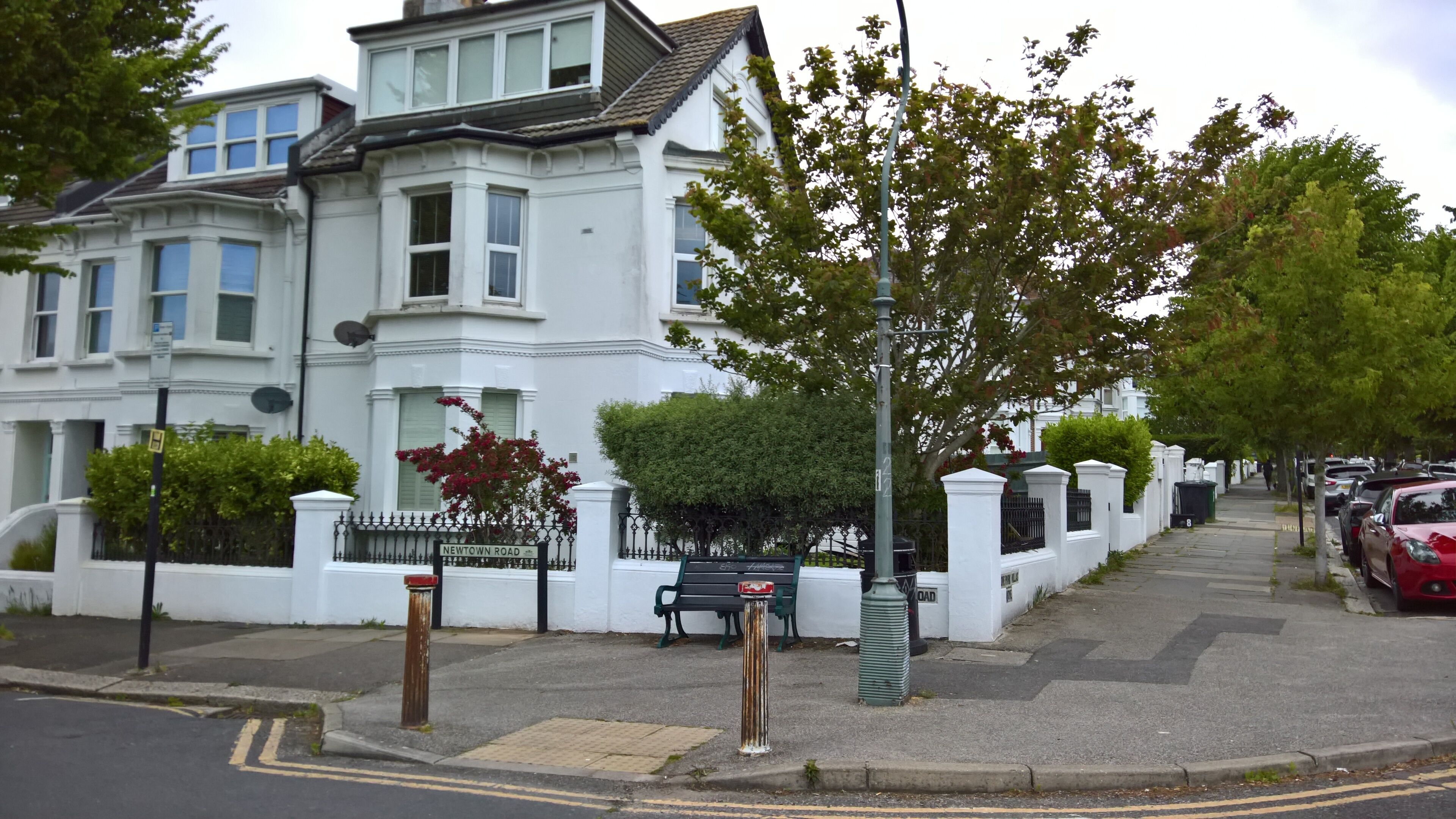 A white building with a gated entrance, a bench, and a street with parked cars.