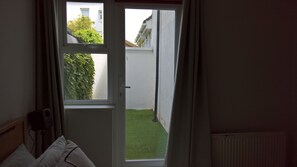 Ein Zimmer mit Fenster zu einer kleinen Außenfläche mit Hecke und weißer Mauer.
