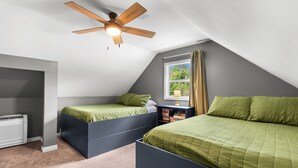 Un dormitorio con dos camas, ventilador de techo, ventana con cortinas y un radiador.