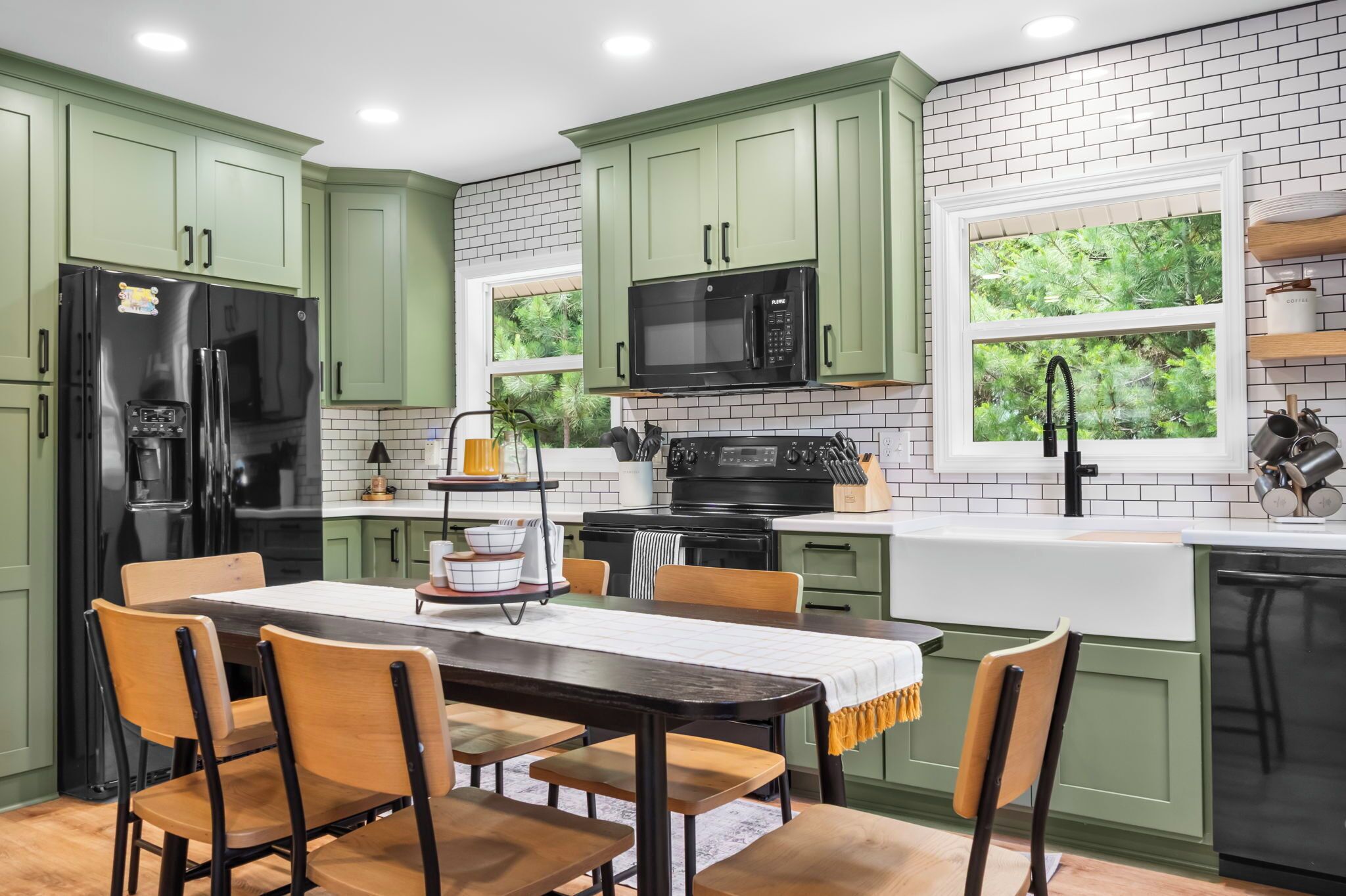 A kitchen with green cabinets, a black refrigerator, a microwave, and a sink.