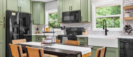 A kitchen with green cabinets, a black refrigerator, a microwave, and a sink.