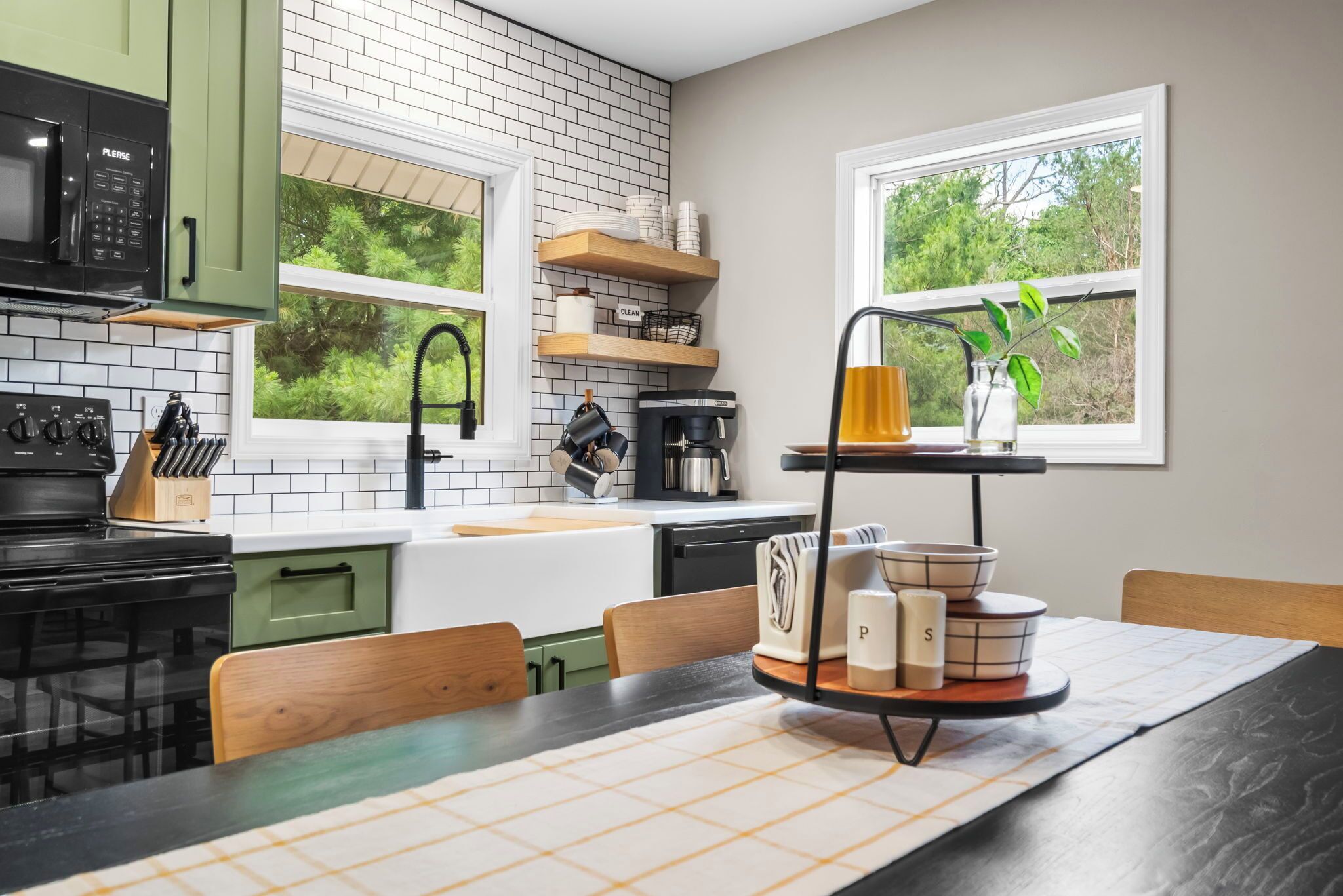 A modern kitchen with a black stove, white tiled backsplash, and a window with a view of greenery.