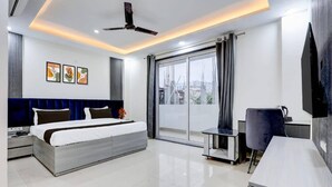 A modern bedroom with a bed, a desk, a chair, a ceiling fan, and a TV.