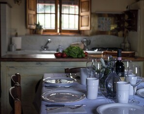 Een eettafel gedekt met borden, glazen en bestek in een keuken met houten kastjes en een raam.