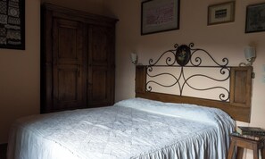 Een slaapkamer met een grote houten garderobe, een decoratief metalen hoofdbord en een nachtkastje met boeken.