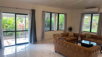 Un salón amplio con un gran sofá, una mesa de centro y vistas a un jardín a través de puertas correderas de cristal.