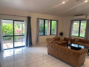 A spacious living room with a large sofa set, a coffee table, and a view of a garden through the sliding glass doors.