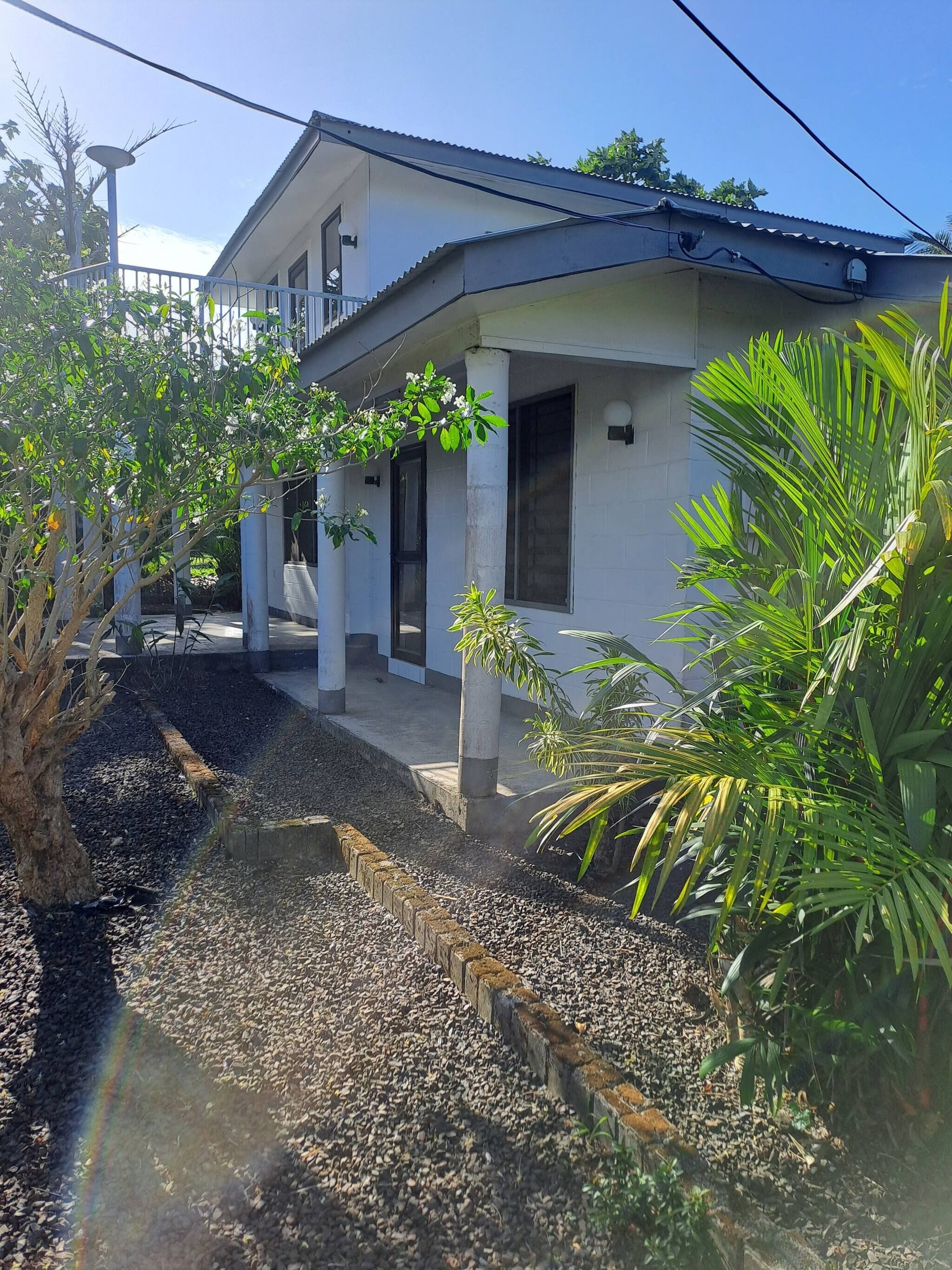A residential building with a covered porch, a garden with gravel paths, and a variety of plants.