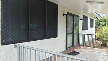 Un'area esterna coperta con ringhiera in metallo, pavimento piastrellato e un edificio bianco con ampie finestre.