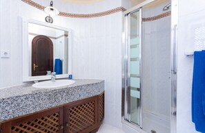 A bathroom with a granite countertop sink, a mirror, a shower with a glass door, and a towel rack. - Apartment in Bahia Feliz by Playa del Aguila (San Bartolomé de Tirajana)