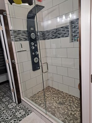Eine begehbare Dusche mit Glastrennwand, Bedienfeld, gefliesten Wänden und einem Musterfliesenboden.