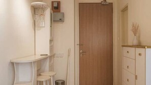 Un pasillo con una puerta de madera, un armario blanco, una mesita con sillas y un cubo de basura.