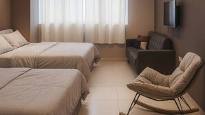 Habitación de hotel moderna con dos camas, una mecedora, un sofá, un televisor de pantalla plana y un ventanal con cortinas.