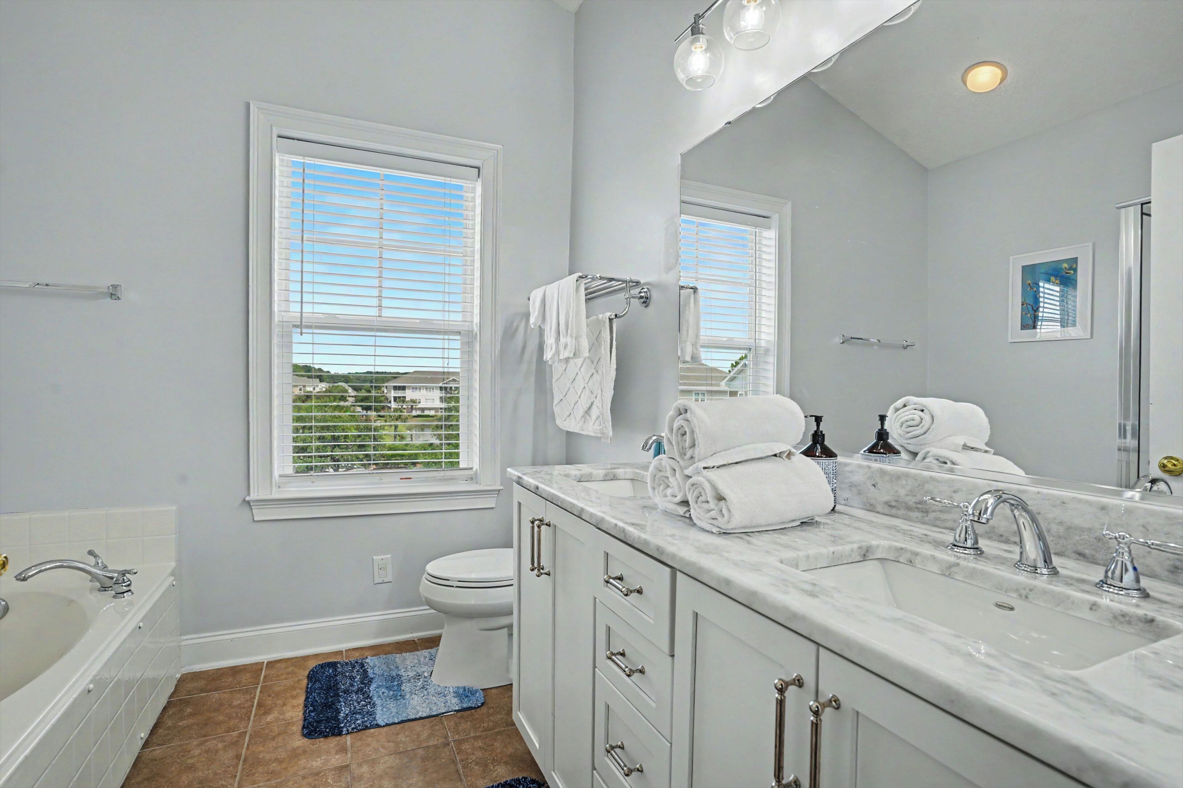 A bathroom with a bathtub, a sink, a toilet, and a window with blinds.