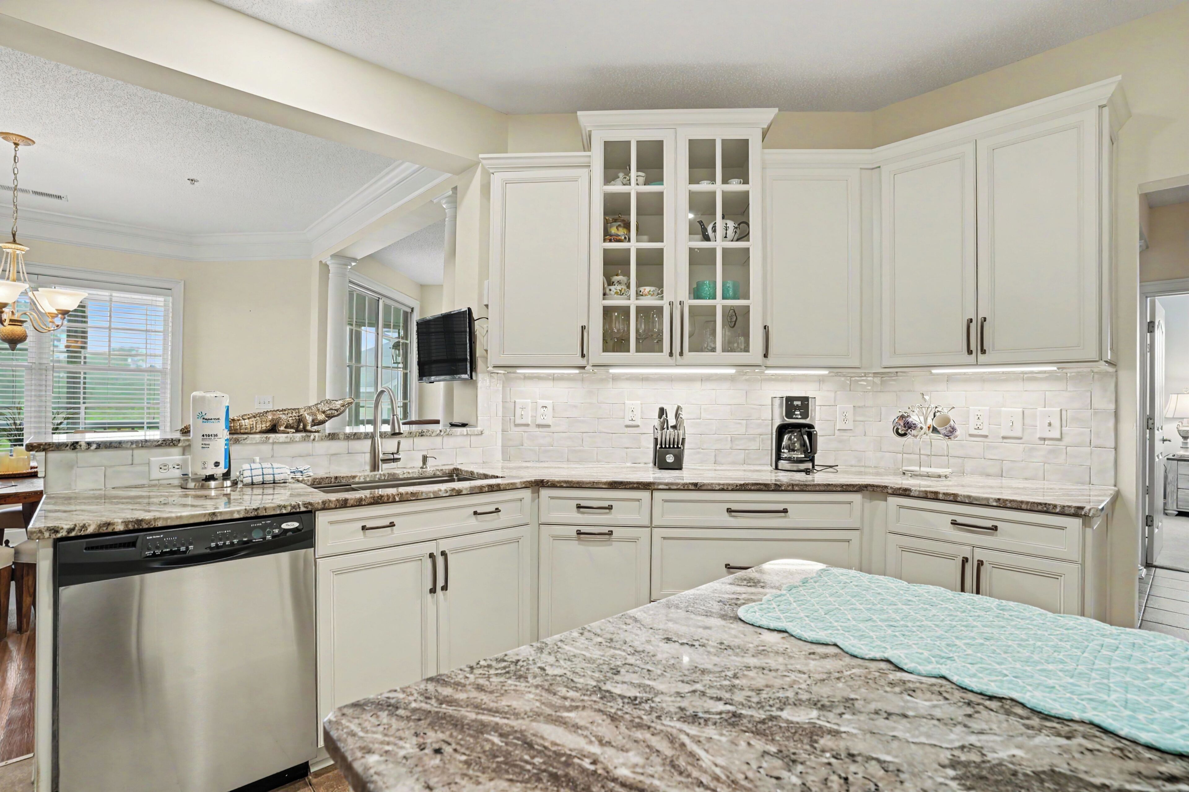 A kitchen with white cabinets, a granite countertop, a dishwasher, and a window with blinds.